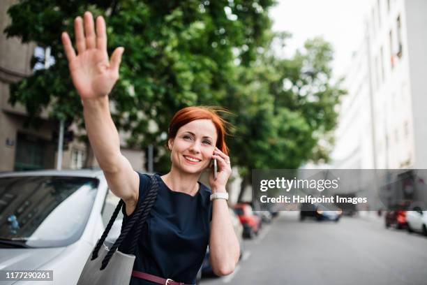 young businesswoman with smartphone standing outdoors in city, hailing a taxi. - waving hand stock-fotos und bilder