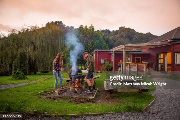 a couple starts a bonfire at the campsite. - cabaña de madera fotografías e imágenes de stock