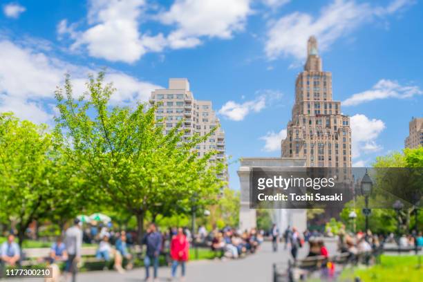 people sit down and relax on the park bench along the footpath beside the fresh green leaf trees in washington square park under the floating clouds in the blue sky at new york city ny usa on may 16 2019. - washington square park stock pictures, royalty-free photos & images