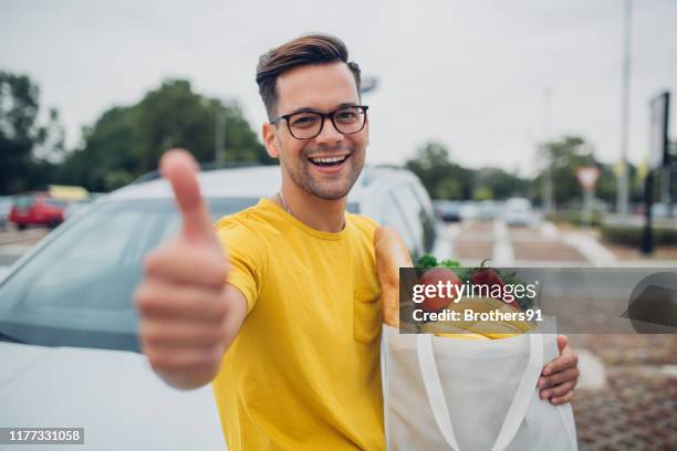 jeune homme retenant des épiceries dans le sac réutilisable et affichant le pouce vers le haut - super aliments photos et images de collection