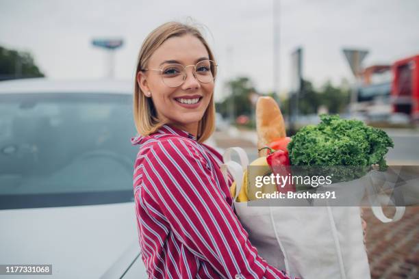 feliz joven sosteniendo comestibles en bolsa reutilizable - woman carrying tote bag fotografías e imágenes de stock