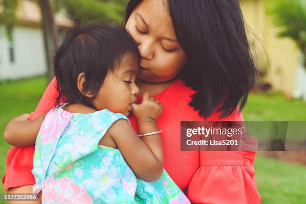 beautiful mother snuggles with toddler daughter in an outdoor portrait - thumb sucking stock pictures, royalty-free photos & images