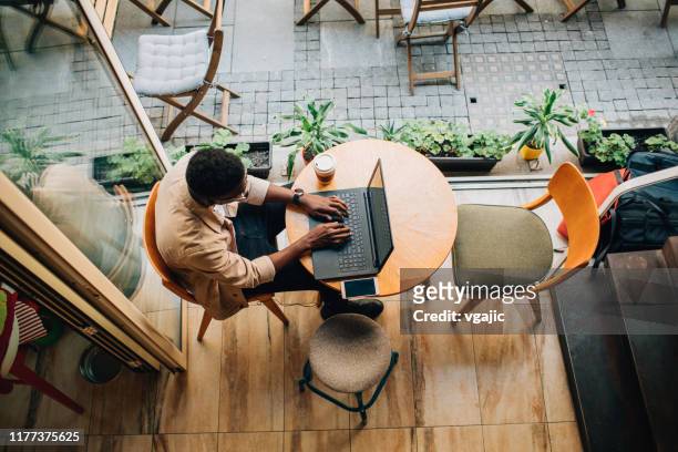 young man sitting in coffee shop and using laptop - city life cafe stock pictures, royalty-free photos & images