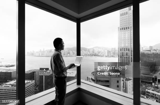 zakenman staande bij het raam en met behulp van laptop - black and white stockfoto's en -beelden