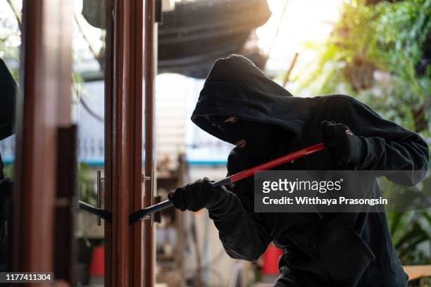 burglar wearing black clothes and leather coat breaking in a house - fagotto foto e immagini stock