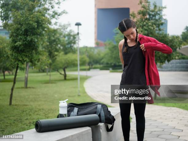 mujer joven poniéndose chaqueta al aire libre - gym bag fotografías e imágenes de stock