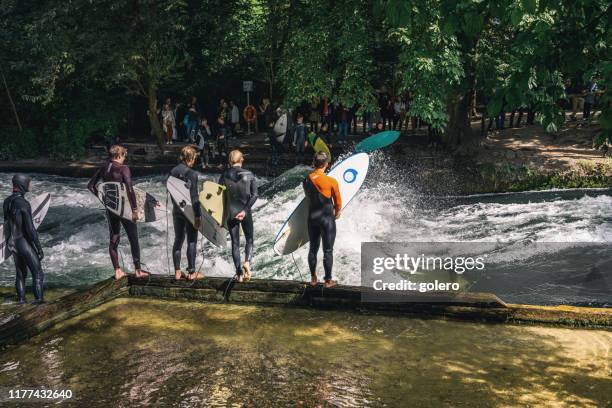 young surfers at the eisbach in the english garden in munich - isar münchen stock pictures, royalty-free photos & images