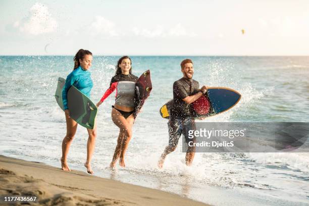 glückliche junge leute laufen an einem strand mit surfbrettern. - beach hold surfboard stock-fotos und bilder