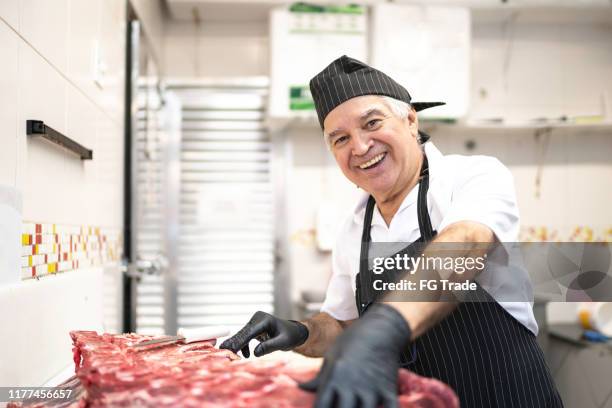 ritratto di macellaio che taglia un pezzo di carne rossa in macelleria - butcher foto e immagini stock