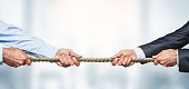 Tug of war, two businessman pulling a rope in opposite directions