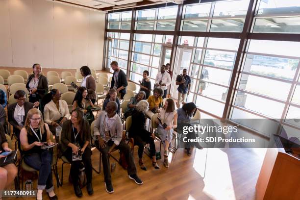 high angle view as conference attendees wait for speaker - town hall meeting stock pictures, royalty-free photos & images