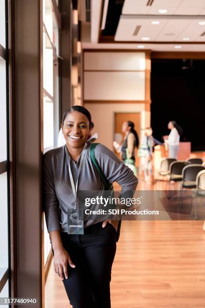 at conference, mid adult woman stands by window and smiles - incidental people stock pictures, royalty-free photos & images