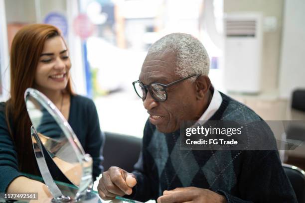 optometrist helping client trying on some glasses - older black people shopping stock pictures, royalty-free photos & images