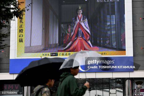 People walk past a screen displaying Japan's Crown Princess Kiko attending the proclamation ceremony of Japan's Emperor Naruhito's ascension to the...