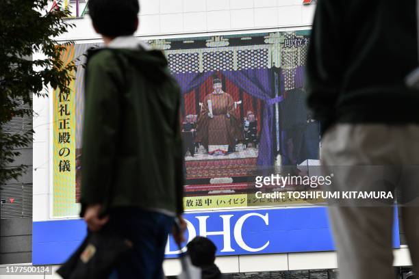 People look at a screen displaying Japan's Emperor Naruhito attending the enthronement ceremony where he officially proclaims his ascension to the...
