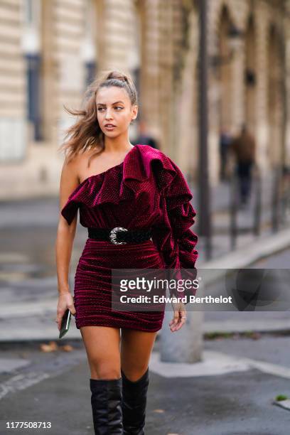 Carla Ginola wears a lustrous burgundy with tiny polka dots frilly one-shoulder gathered mini dress, a black belt with a silver buckle, black...