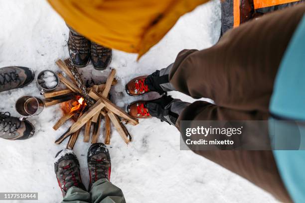 tourists warming by campfire on snow - outdoor footwear stock pictures, royalty-free photos & images
