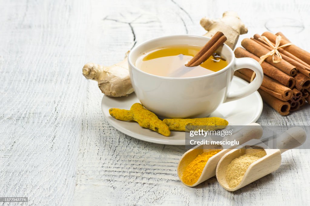 Herbal ginger and turmeric tea in white cup with ginger root, dry turmeric, cinnamon sticks and their powder