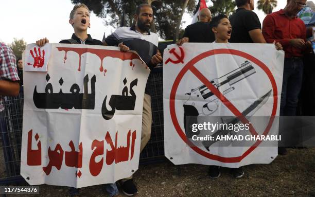 Arab Israeli protesters carry a placard reading in Arabic, "enough with violence, arms are destroying us" as they protest outside the district police...