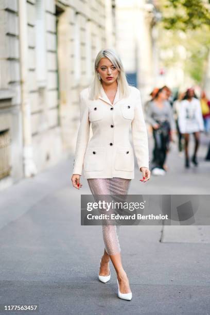 Caroline Vreeland wears earrings, a cream-color jacket with pockets and black buttons, a glittering see-through mesh pencil skirt, white pointy heels...