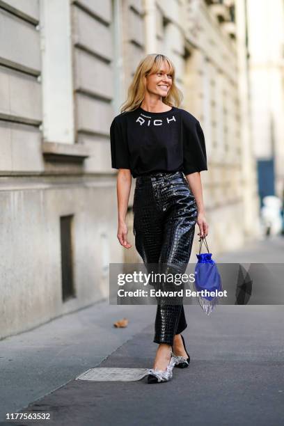 Jeanette Madsen wears earrings, a black Alessandra Rich t-shirt, shiny black crocodile pattern high waist leather pants, a blue fringy bag, black...