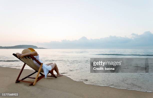 femme détendant sur la présidence de plate-forme à la plage - couché de soleil photos et images de collection