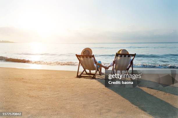 couple sitting on deck chair at beach - beach relaxation stock pictures, royalty-free photos & images