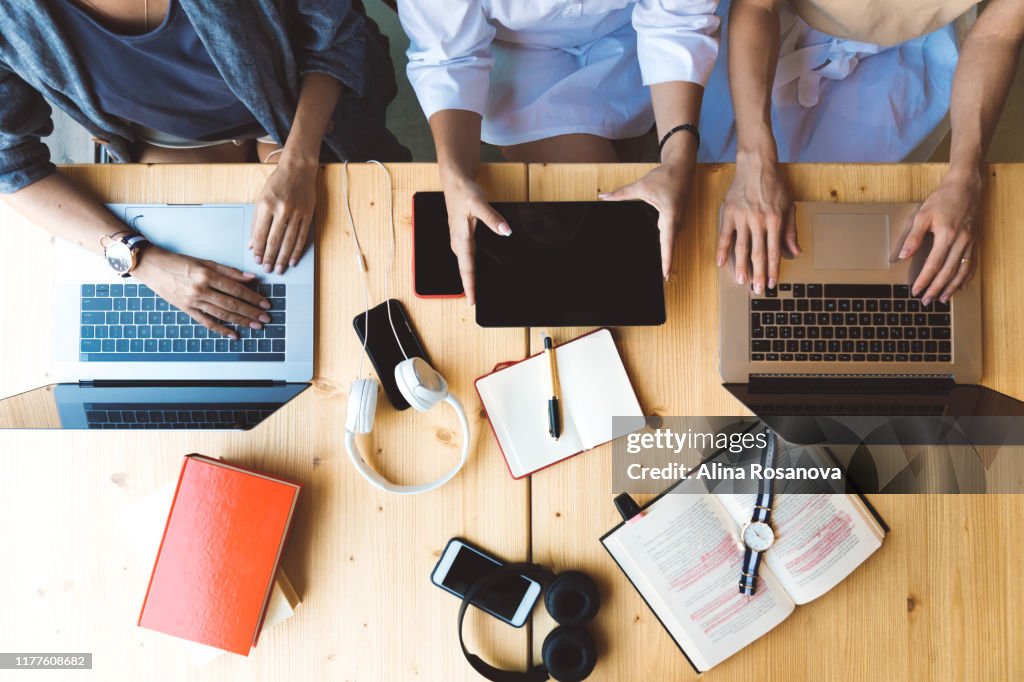 Flat lay picture of three women working with laptops and books sitting at the table together - business woman, co-working and college girls studying concept
