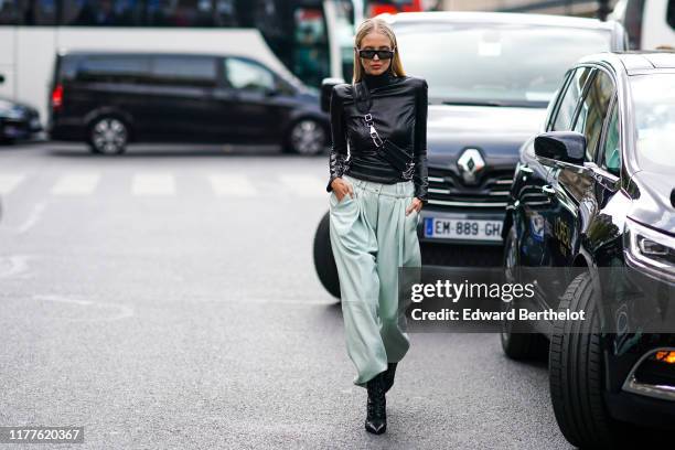 Leonie Hanne wears sunglasses, a black leather top, a small shoulder strapped fanny pack bag, pale green pants, black shoes, outside Balmain, during...