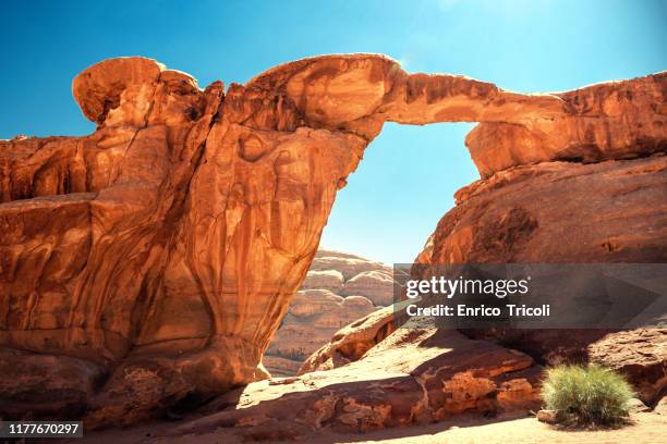 jordan: rock bridge in the wadi rum desert; very warm colors on yellow and red during sunset. background, wallpaper. - rotsformatie stockfoto's en -beelden