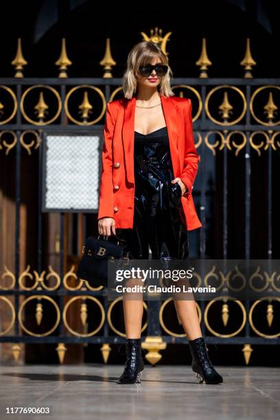 Xenia Adonts, wearing an orange blazer, black top, black vynil shorts, black boots and black Balmain bag, is seen outside the Balmain show during...