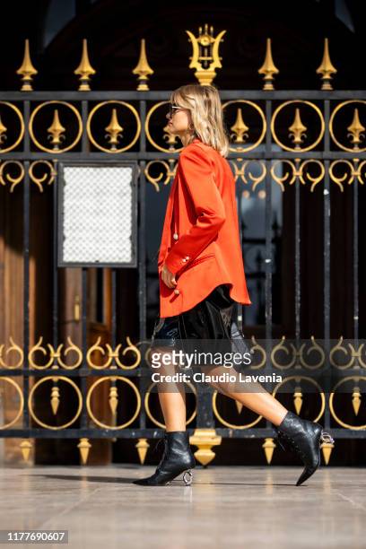 Xenia Adonts, wearing an orange blazer, black top, black vynil shorts, black boots and black Balmain bag, is seen outside the Balmain show during...