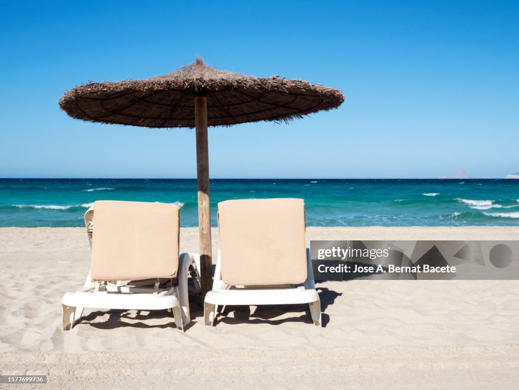 White sand beach with  beach umbrellas & sun loungers  against clear blue sky in Formentera island, Spain.