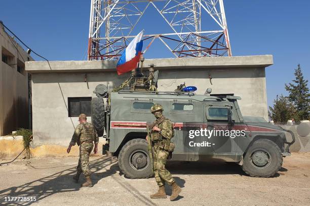 Russian soldiers walk past a Russian military police armoured vehicle at a position in the northeastern Syrian city Kobane, also known as Ain...