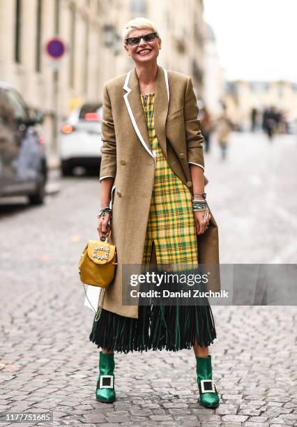 Guest is seen wearing a beige coat, and a yellow and green plaid dress with a yellow bag and green boots outside the Altuzarra show during Paris...