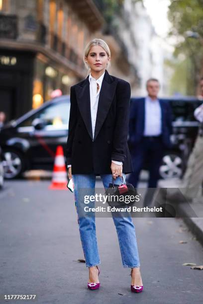 Caroline Daur wears a white shirt, a black blazer jacket, a bag with an attached pink mini bag, blue cropped jeans, purple shoes, outside Ralph...