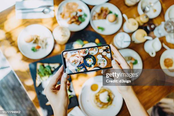 directly above view of woman's hand taking photo of freshly served brunch with smartphone in an outdoor restaurant against beautiful sunlight - hotel breakfast stock pictures, royalty-free photos & images