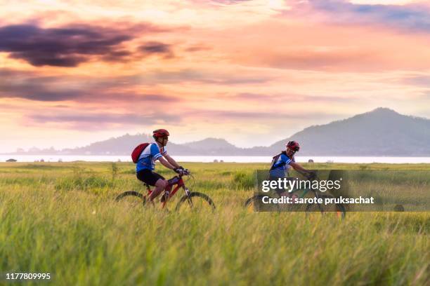 asian couple cycling on the countryside with  sunset sky . - landschaft asien schiene stock-fotos und bilder