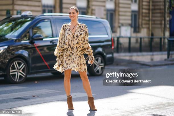 Beatrice Valli wears a V-neck beige and brown spotted gathered and flowing mini dress with long sleeves, brown pointy heeled ankle-boots, outside...