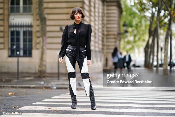 Taylor Lashae wears a black long sleeves top with a lavaliere, a black lace bra, a black leather crop pants with white leather inserts, embossed...