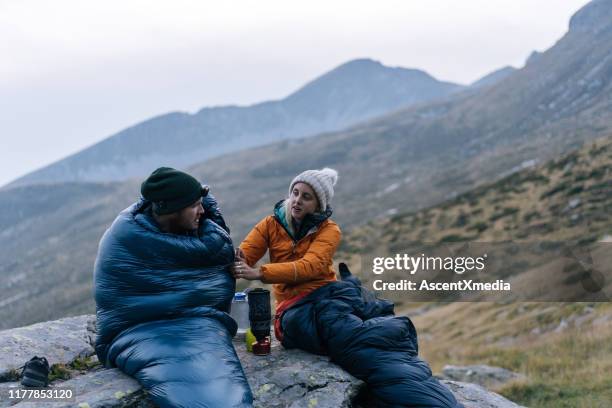 pareja acampando sin tienda de campaña preparar una bebida caliente - saco de dormir fotografías e imágenes de stock