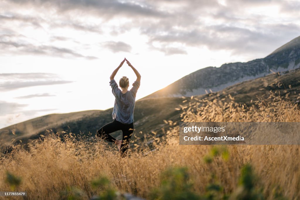Mujer joven preforma yoga en las montañas a la luz de la mañana