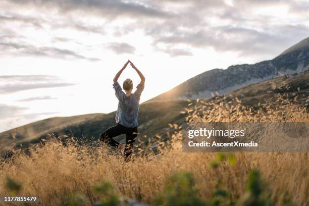 jonge vrouw preforms yoga in bergen in ochtend licht - op een been staan stockfoto's en -beelden