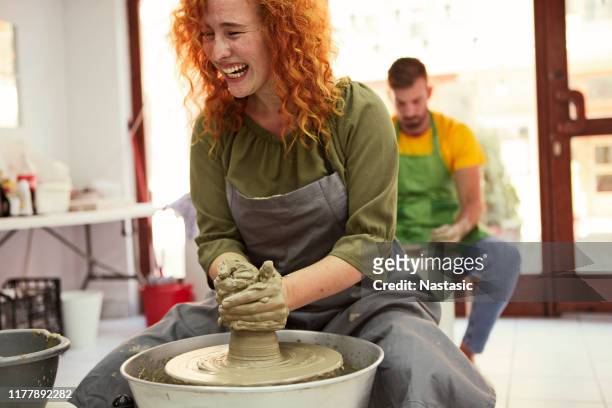 femme rouge de cheveux souriant dans la poterie faisant l'argile de moulage de studio - pottery wheel photos et images de collection
