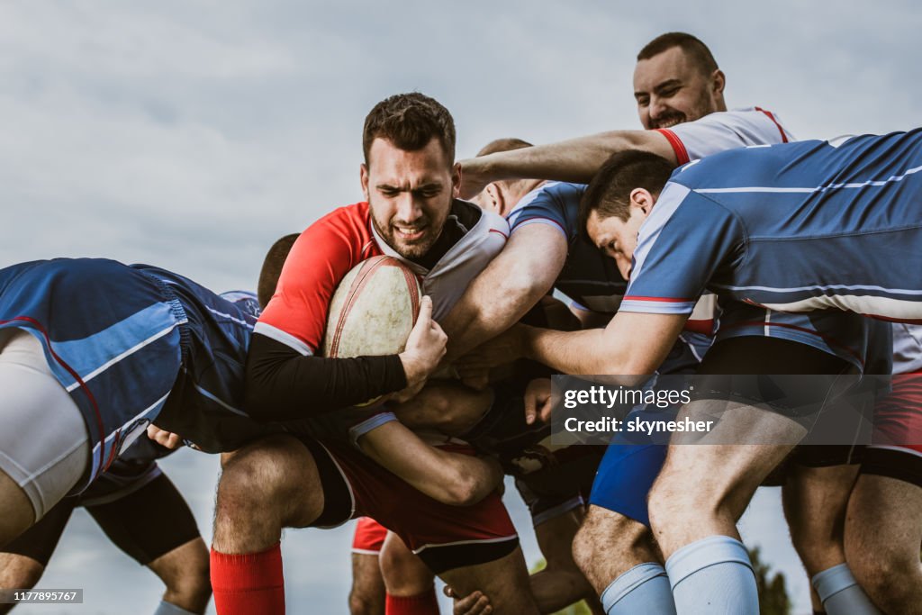 Rugby players blocking their opponent on a match at playing field.