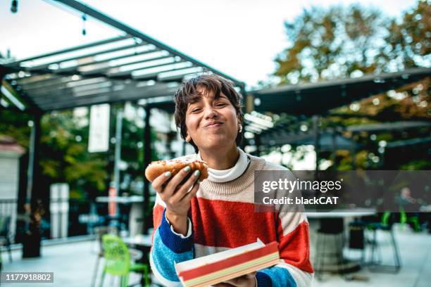 giovane donna che mangia hot dog per strada - take out food foto e immagini stock