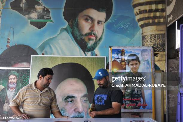 Iraqi men work in front of posters bearing the portraits of Iraqi Shiite cleric and political leader Moqtada al-Sadr , Grand Ayatollah Ali Sistani ,...