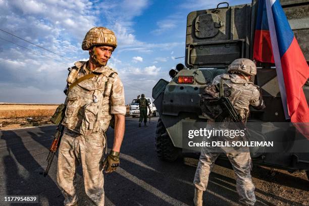 Russian military police members stand outside an armoured personnel carrier along a road in the countryside near the northeastern Syrian town of...