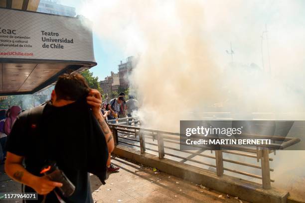 Protester protects his face from smoke billowing from the entrance of a subway station as people demonstrate in the streets of Santiago on October...