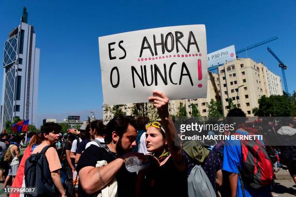 Man holds a sign reading "It's Now or Never" as people demonstrate in the streets of Santiago on October 24, 2019 after a week of street violence...